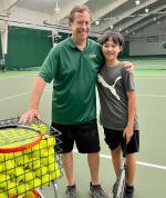 Patrick Page and student standing on court with ball cart and racquet
